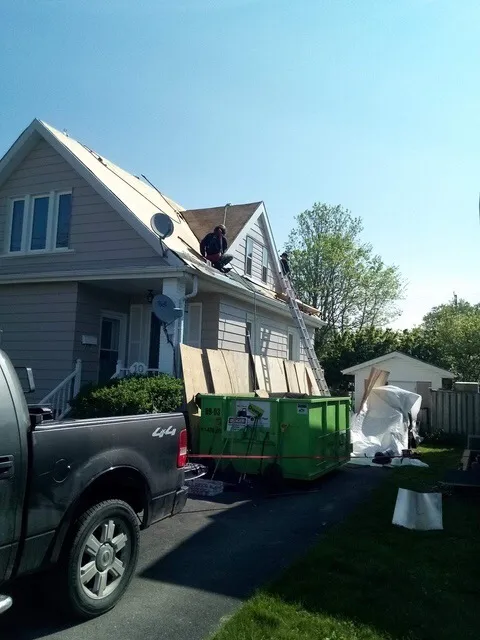 Heisler & Sons crew stripping a roof, with the dumpster in the driveway