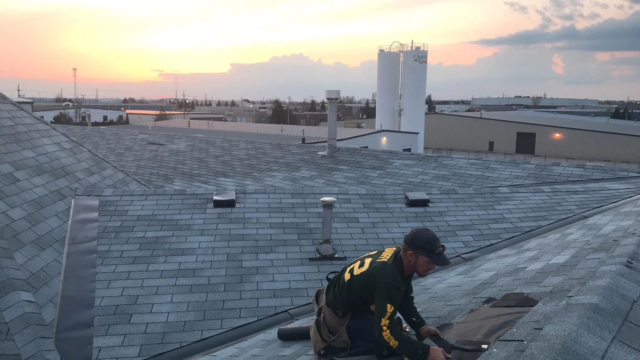 A Heisler & Sons roofer working on a shingle roof at sunset
